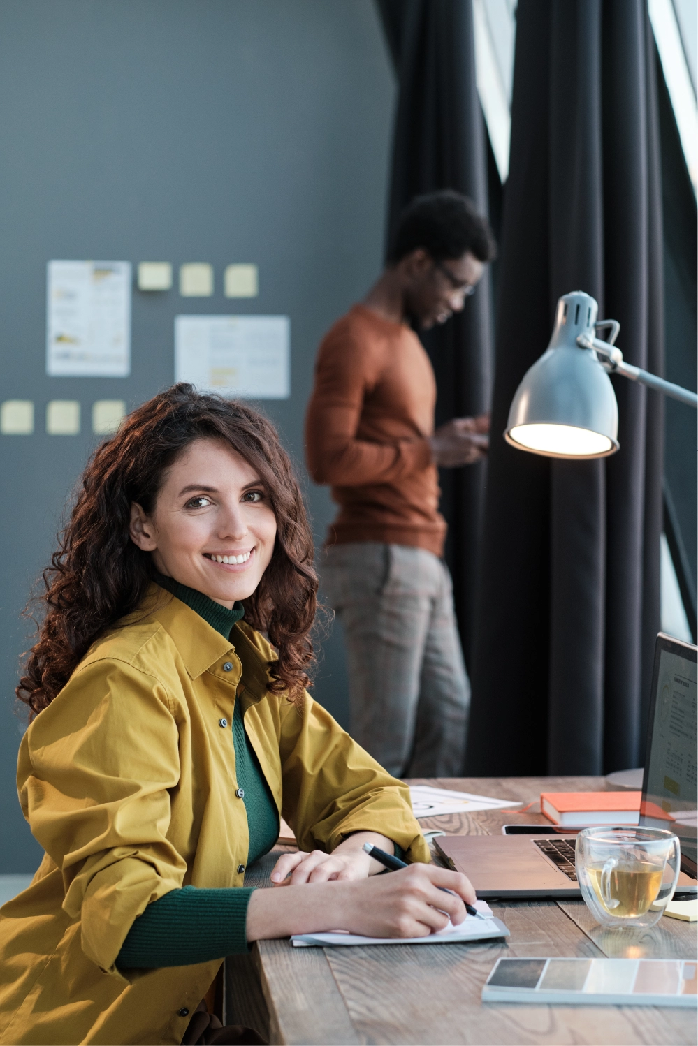 Frau sitz im Büro am Schreibtisch und lächelt in Kamera